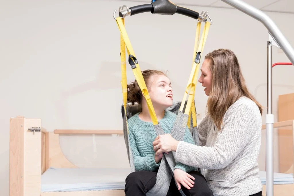 Support worker with disabled woman with complex needs in disability sling